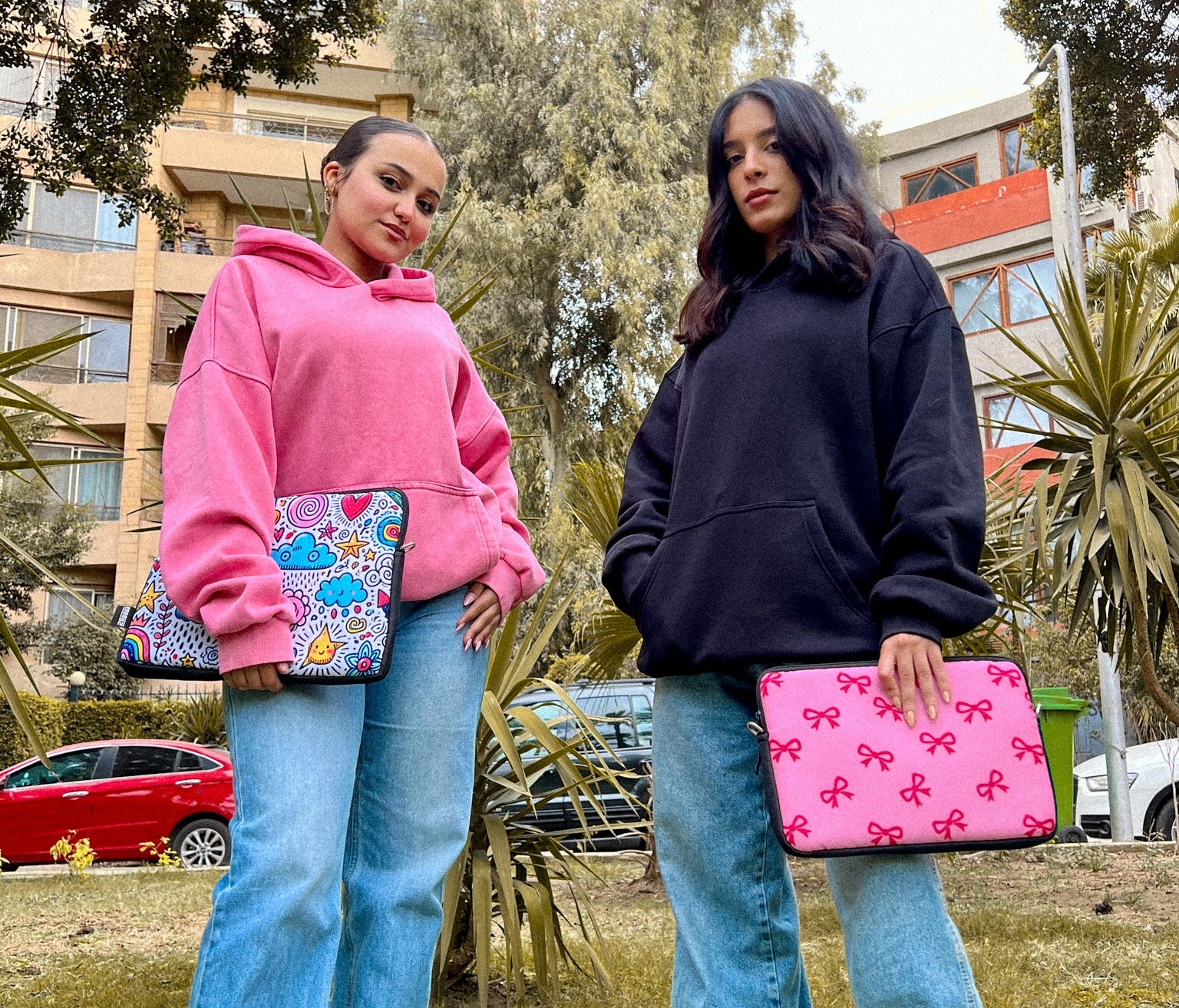 Two people standing outdoors, wearing matching outfits with colorful bags.